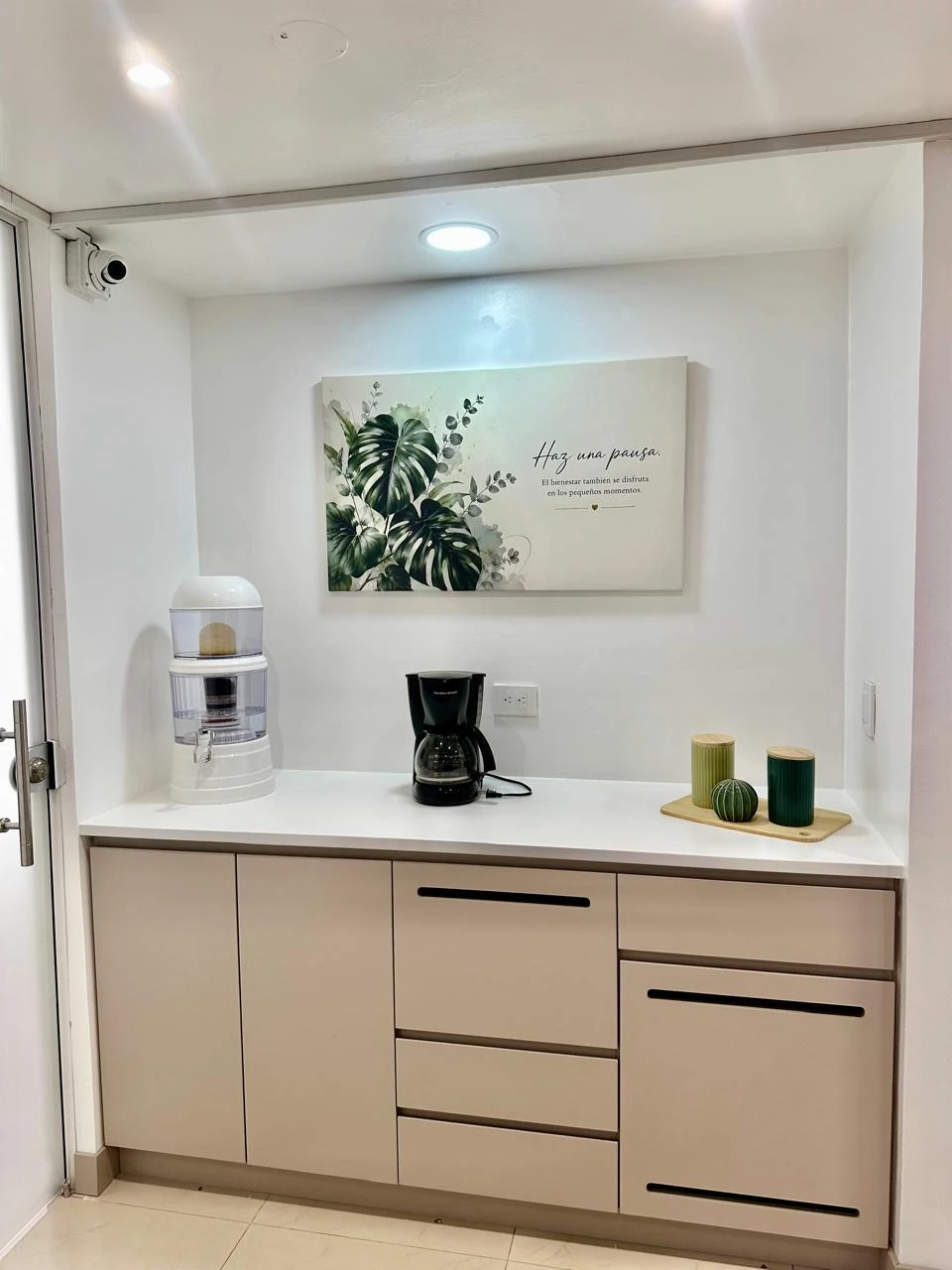 Zona de café de Medical Center 125 con dispensador de agua, cafetera y muebles de apoyo.